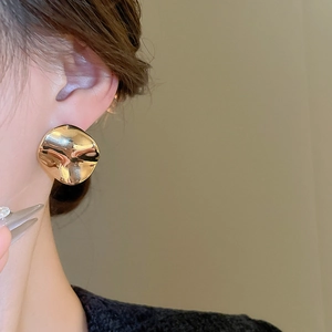 Close-up of a model wearing minimalist irregular gold wavy metal disk earrings