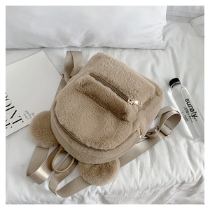 Macro detail of khaki plush backpack featuring cute pom-pom ears and a front zipper pocket