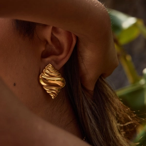 Close-up of a gold shell-shaped earring on model with detailed spiral texture
