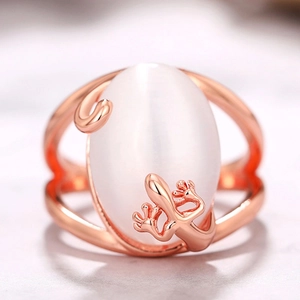 Close-up of rose gold gecko ring featuring a large white cat eye stone on marble surface