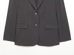 Detail of charcoal grey blazer featuring a two-button closure and classic flap pockets