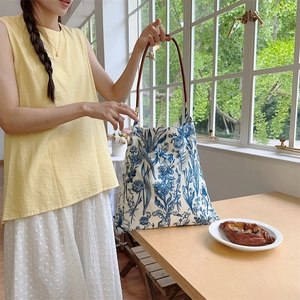 Blue floral canvas tote bag with brown leather handles on a minimal wooden table