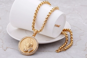 Macro detail of golden praying hands medallion with rhinestones on a box chain