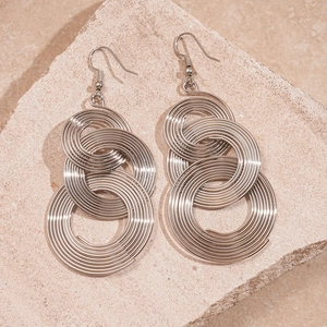 Detailed macro view of silver geometric spiral tassel earrings on a textured stone base