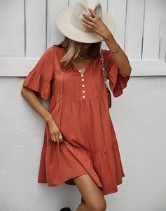 Détail d'une robe courte orange à col en V avec boutons blancs et jupe à plusieurs niveaux