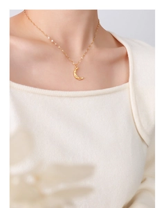 Golden crescent moon pendant necklace worn on a white knit sweater in a soft aesthetic