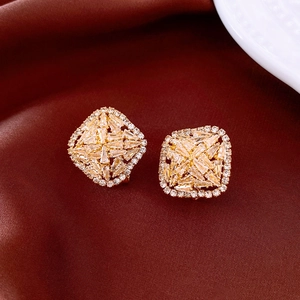 Detailed close-up of square zircon stud earrings with gold plating on red silk background