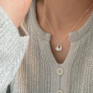 Close-up of a silver fluid texture heart pendant necklace worn on a model's collarbone