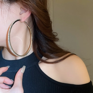 Side view of a large gold-plated hoop earring with pavé rhinestones worn by a model