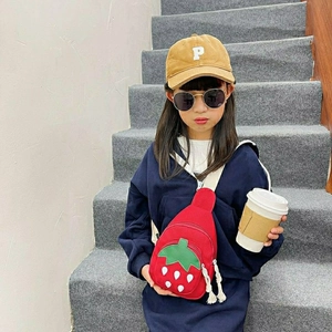 Cute red strawberry canvas crossbody bag for girls shown on a child model outdoors