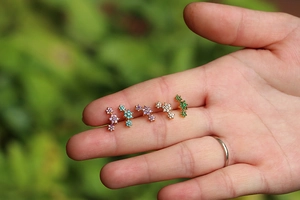 Detailed close-up of colorful flower petal stud earrings held in hand against nature