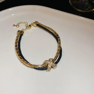Détail d'un bracelet double couche plaqué or avec breloque en forme de X sertie de zircons