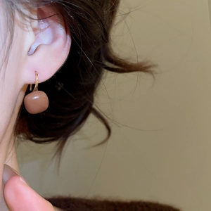 Close-up of C-shaped square tiger eye earrings with gold hooks worn by a model