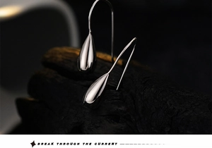 Macro shot of silver teardrop earrings on black charcoal texture showing mirror reflection