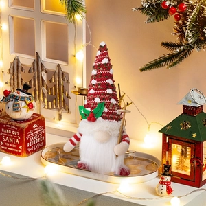 Close-up of a festive knitted Christmas gnome holding a wooden staff with holly leaves