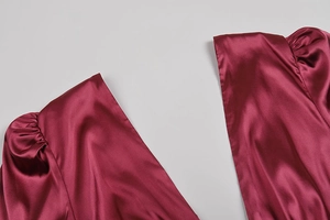 Dettaglio dell'abito in raso rosso vino con scollo a V e maniche a sbuffo a pieghe