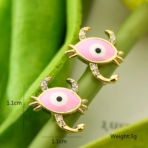 Detailed macro view of 18K gold plated crab evil eye stud earrings with pink enamel