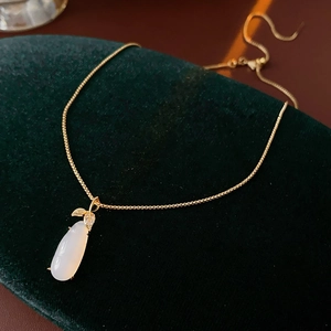 Detail of gold-plated leaf pendant with white chalcedony and zircons on silk background