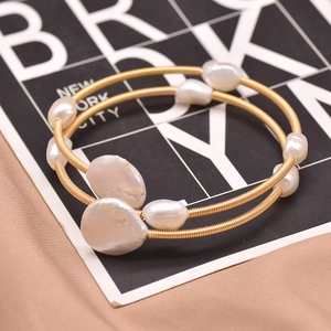 Detail of golden spiral wrap bracelet with white baroque pearls on elegant fabric