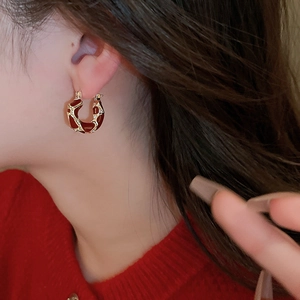 Close-up of vintage U-shaped gold earrings with red enamel and diamonds on a model