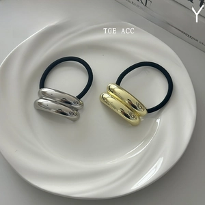 Close-up of gold and silver minimalist geometric metal tube elastic hair ties in a dish