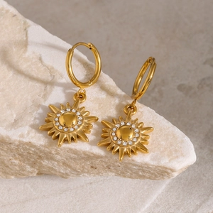 Detailed macro view of golden sun pendant earrings with sparkling crystals on stone texture