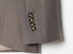 Detail of suit jacket cuff with four dark buttons on brown twill fabric