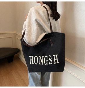 Detail of a large black canvas tote bag with brown handles and white logo on a model