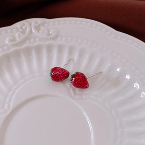 Close-up of strawberry stud earrings with red drip glaze on white ceramic plate