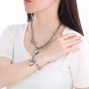 Model wearing a chunky stainless steel heart pendant necklace and bracelet set with OT clasp
