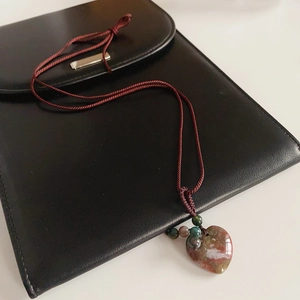 Detailed close-up of heart-shaped stone pendant on dark red braided sweater chain