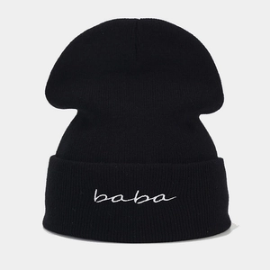 Close-up of thick black knit beanie featuring white baba embroidery on the folded cuff