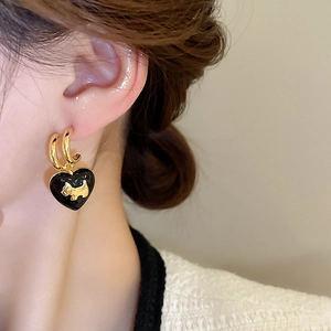 Detail of heart drop earrings with gold puppy motif worn by a model in soft lighting