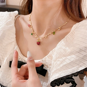 Close-up of a red glass strawberry pendant with a gold chain worn on the neck