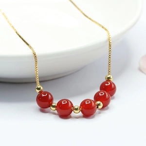 Collier en agate rouge naturelle avec perles dorées sur plateau blanc pour style chic