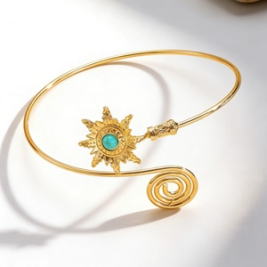 Macro detail of golden sun-shaped arm cuff with a turquoise stone inlay and spiral design