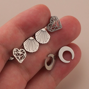 Macro detail of three minimalist stainless steel studs in heart, shell, and crescent shapes