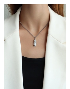 Detail of silver oval embossed pendant necklace worn over a professional black and white outfit