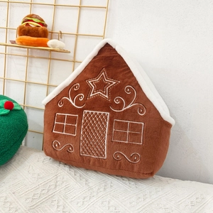 Close-up of a gingerbread house plush pillow with white embroidery on soft brown fabric