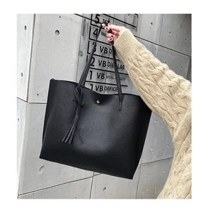 Close-up of black litchi grain leather tote bag featuring tassel detail and gold magnetic buckle