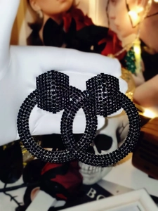 Detail of vintage black rhinestone double hoop earrings held by a gloved hand