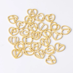 Close-up of golden heart-shaped pendants with hollowed-out alphabet letters on white surface