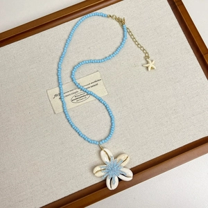 Detail of blue beaded necklace featuring a shell flower pendant and starfish charm