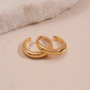 Close-up of minimalist gold C-shaped ear cuffs on a textured warm beige surface