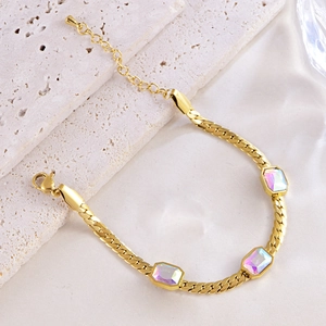 Golden snake chain bracelet with three rectangular iridescent gemstones on stone background