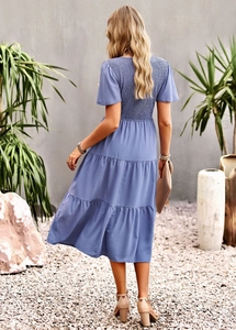 Back view of a blue short-sleeve tiered dress with a cinched waist in an outdoor setting