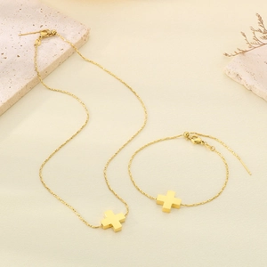 Detailed view of golden cross pendant necklace and bracelet set on a textured surface
