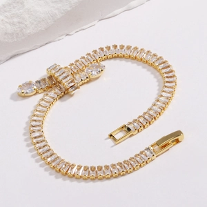 Gold tennis bracelet with rectangular zircons and pear-shaped drop charms on white base