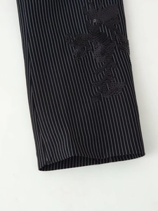 Détail de la broderie à paillettes noires sur le tissu rayé de la manche d'un tailleur