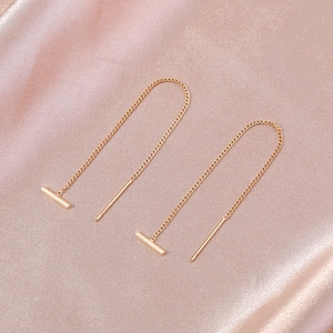 Macro detail of elegant gold-tone threader earrings with T-bar drops on pink satin